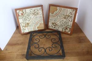 lot 36 image: 2-vintage-style trivet featuring a square ceramic tile with a decorative floral pattern set within a wooden frame. One is missing a foot see pictures & black wrought iron trivet features a rustic scrollwork pattern with sturdy legs.