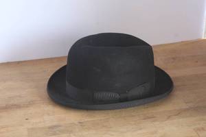 lot 42 image: This black felt Homburg hat features a distinctive curled brim and a grosgrain ribbon band with a small bow