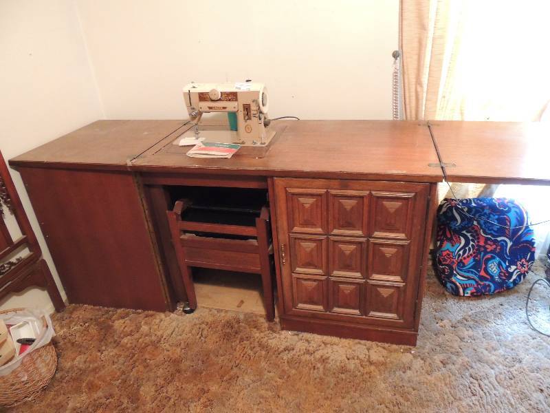 lot 272 image: Sewing table with singer sewing machine. Table has drop side for additional area cabinet has 5 drawers sewing chair with storage. Back folds for storage in cabinet