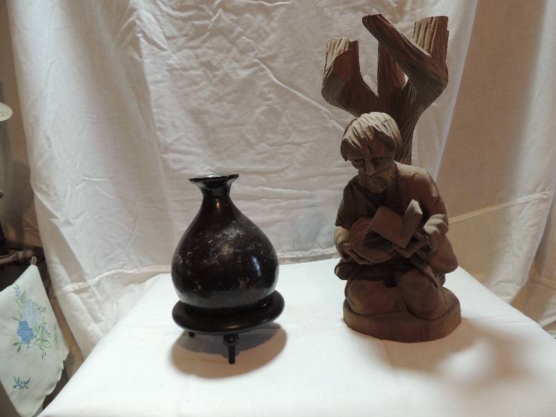 lot 296 image: Carved man reading book under tree 13 H and black pot  vase 6 in stand. Don�t know the name of the book, does it matter