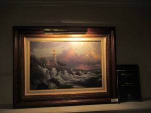 lot 3 image: THOMAS KINKADE CONQUERING THE STORMS SEA SIDE MEMORIES VI. LIMITED EDITION LITHOGRAPH WAS ADDITIONALLY HIGH-LIGHTED BY A THOMAS KINKADE MASTER APPRENTICE. INCLUDES COA AND ORIGINAL RECIEPT. MEASURES 28 X 22