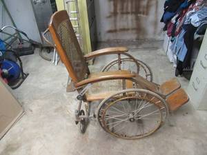 lot 277 image: ANTIQUEVINTAGE 1930S WOOD AND WICKER SEAT WHEEL CHAIR THAT EXTENDS FLAT WITH 4 WHEELS. SEAT HAS REPAIR.