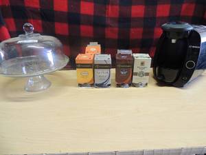lot 172 image: Bosch single cup coffee maker with various boxes of coffee pods and a cake plate and dome