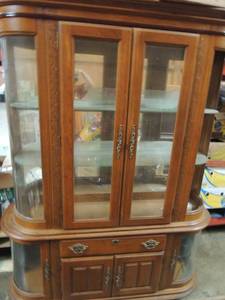 lot 695 image: Large curio cabinet 1 side oval piece broken lighted with 4 knights 1 drawer double doors at bottom, double doors at top and 2 inside glass shelves bottom on each side has 1 glass shelf with door 1 shelf