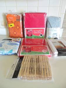 lot 64 image: NIP nonslip mat, 5 NIP table cloths (red, white, fall, fish) and NIP 50 wooden clothes pins