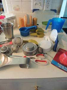 lot 14 image: Kitchen lot- measuring spoon set, measuring cup set, spoon rest, scissors, tea infuser x 4, wooden napkin holder with S&P scoops and  small cutting board 4x8
