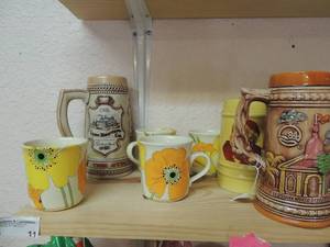 lot 11 image: Lion brewing stein from Detroit MICHIGAN , Wonder Wall stein made in Louisiana 1984,  Yellow Santa stein,  4 coffee cups with orange and yellow flower dcor