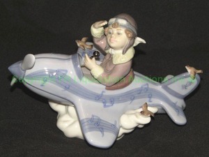 lot 325 image: Lladro over the clouds 5697 boy blue airplane, (wing on one bird is broken)