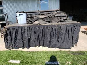 lot 57 image: Metal Legged Wood Stage 384 Square Feet Total, 8 x 4 Stage pieces with legs and clamps, has 2 pieces of black astro turf carpet to cover it