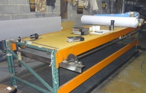 lot 294 image: Industrial table w built-in motorized roller, rack and counter.  Currently used for measuring and rolling fabric & carpet.