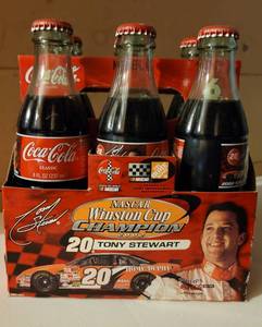 lot 85 image: Six pack of 2002 Tony Stewart #20 Nascar Winston Cup Champion commemorative Coca-Cola bottles with carton as shown.