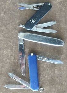 lot 143 image: Three knives one is silver tone and made in Germany, the other two are Victorinox key chain knives blue and black, (One Money)