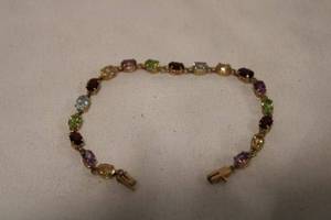 lot 468 image: 10K yellow gold and multi gemstone bracelet. Marked 10K. 18 cttw approx. Includes Amethyst, Blue Topaz, Tanzanite, Peridot, Garnet. 7L with hidden box clasp and safety catch.
