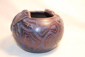 lot 324 image: Amazonian Pottery Artisan crafted by natives in Amazon Rainforest in Brazil. Depicting blue tree frogs and blue incising on brown bowl.  6W x 5H approx. label on bottom.