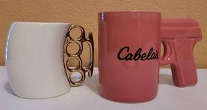lot 12 image: NOVELTY MUGS IN WEAPON FORM. INCLUDES CABELAS PINK MUG WITH GUN HANDLE AND BRASS KNUCKLES MUG