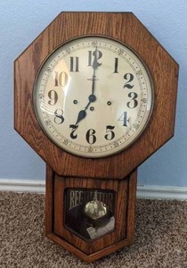 lot 27 image: Pendulum Regulator Wall Clock with key. Clock is about 25 inches tall by 4 inches wide.
