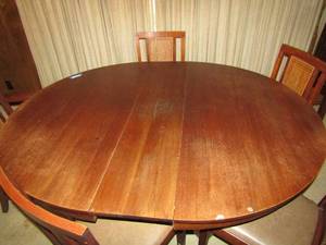 lot 118 image: Mid Century Modern Wood w Wicker inserts Oval dining table and 5 chairs and 1 leaf, Damage to seat of captain chair   without leaf 54x54x25.  has 5 leaves with it in storage box - each is 11W  With all 5  leaves 54 x109 x25