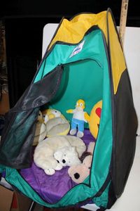 lot 213 image: Toy Lot Play Hut, Bart Simpson Slippers and Toy, Heart Emoji Pillow, Spa Comforts Neck Bear and Cozy Hugs Dog