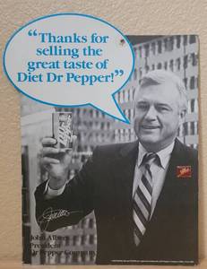 lot 10 image: VINTAGE 1986 DR. PEPPER JOHN ALBERS - PRESIDENT ADVERTISING CARDBOARD SIGN WITH LAPEL PIN IN STYLE SHOWN. APPROX. 9.25 W x 12 H.