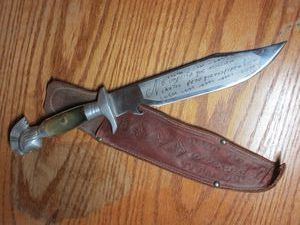 lot 44 image: BOWIE KNIFE W SPANISH WRITING AND AZTEC STYLE WARRIOR ON HANDLE, INCL. LEATHER SHEATH
