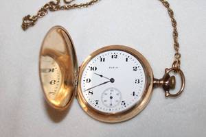 lot 122 image: Elgin pocket watch on 10L chain. Model #8025575 on inside lid. No crystal. Hinge mechanism works. Both exterior sides has vintage Victorian design.