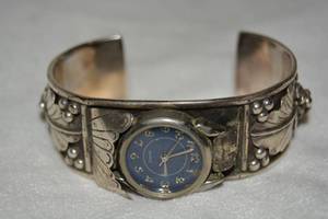 lot 592 image: Signed Sterling Silver S. Ray (Navajo) watch band with quartz watch. Marked Sterling S. Ray. 2.75 opening. Adorned with figural grape vine and leaf motif.
