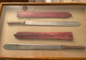 lot 12 image: Shadow box contains 2 handmade African  knifes with cases  MADE BY THE MAISSA TRIBE  - OBTAINED FROM THE KING OF THE TRIBE  25 x 15