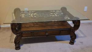 lot 79 image: GLASS TOP WOODEN COFFEE TABLE WITH INTRICATE CARVED DESIGN AND WROUGHT IRON ACCENT AS SHOWN. TABLE HAS ONE DRAWER. MATCHES LOTS #78 AND 80. APPROX. 42.5 L x 26 W x 20 H.