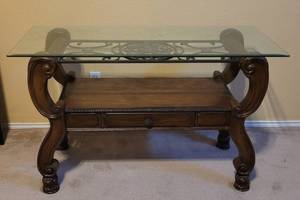 lot 80 image: GLASS TOP WOODEN SOFA TABLE WITH INTRICATE CARVED DESIGN AND WROUGHT IRON ACCENT AS SHOWN. TABLE HAS ONE DRAWER. MATCHES LOTS #78 AND 79. APPROX. 42.5 L x 18 W x 29.5 H.