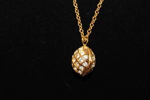 lot 407 image: Signed Joan Rivers crystal adorned egg pendant  locket on a separate 30L gold tone chain. Has jewelry hang tag. Egg locket open to expose a crystal bee inside.