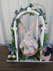 lot 79 image: White lettuce swing with a bunny swinging, decorated with flower water pot, eggs, and greenery dcor, 1614