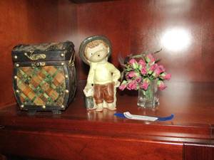 lot 87 image: Wicker basket with latch full of black dcor rocks stones, mini flower case with purple flowers, little porcelain boy no name