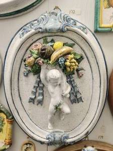 lot 172 image: Handmade oval wall art of raised baby shouldering a cornucopia of fruits (21 x 26). Sticker of authenticity shows origin as Florence, Italy