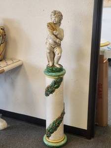lot 89 image: Adorable baby statuary sits atop slender ceramic stand adorned with wrap-around fruit garland (51H, Baby-20H)